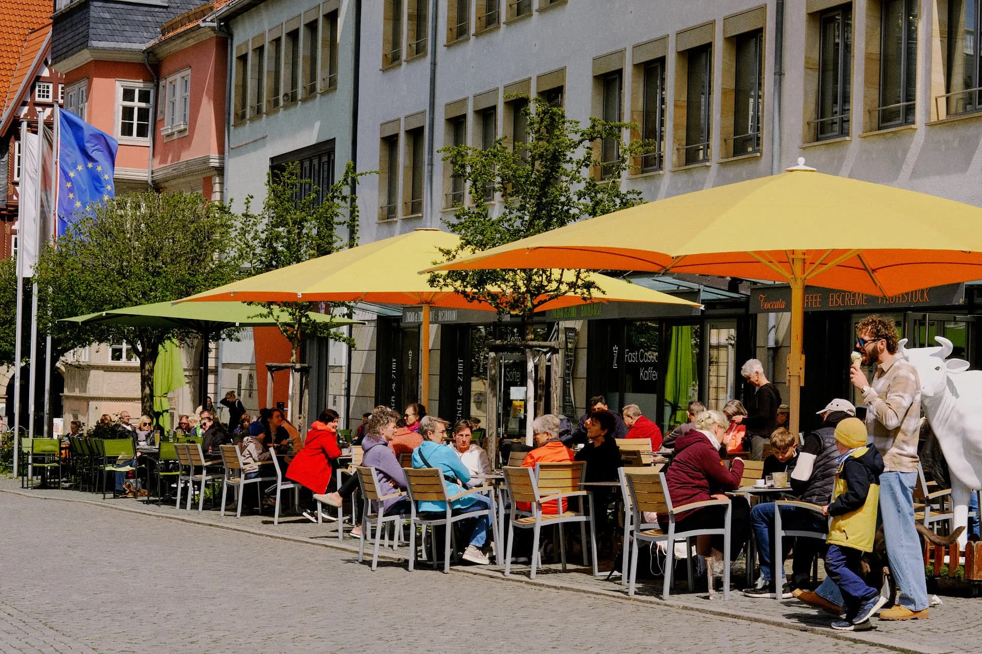 Café Toccata Terrasse am Eisenacher Marktplatz mit gelb-orangen Sonnenschirmen und Gästen